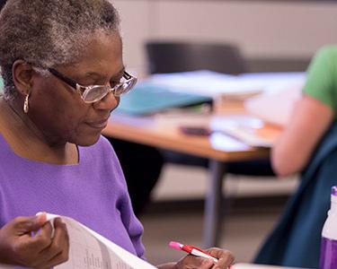 Adult student with pen in hand reading a workbook in class.